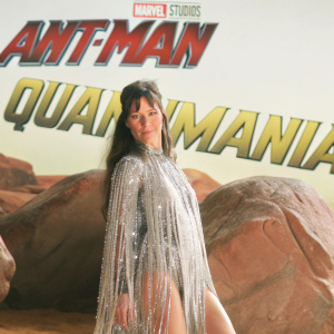 Evangeline Lilly, dressed in a shimmering, fringed costume, poses dramatically on set of Ant-Man and the Wasp: Quantumania. Behind her, the film's title looms large on a Marvel Studios backdrop.