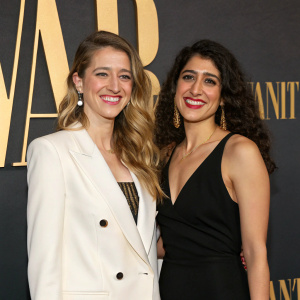 Kate Slesinger and Zeina Dakak attend the Vanity Fair Oscar Party. Both are smiling, Kate in a white blazer, Zeina in a black dress. Dark backdrop with gold accents.