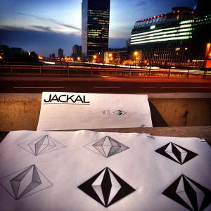 Design sketch of 'Jackal' logo. Sleek black and white geometric shape. Various stages of creation. Brightly lit urban backdrop