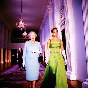 Queen Elizabeth II and Jennifer Lopez at the Golden Globe Awards. Both are in formal attire. Queen in a light blue dress, Lopez in a green gown. Indoor setting, elegant, with warm lighting.