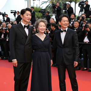 Kim Kang-Woo, Kim Hyo-jin, Youn Yuh-jung, and Baek Yoon-sik at Cannes Film Festival. Red carpet event. Flashing cameras and paparazzi in the background.