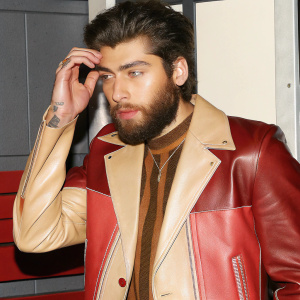 Close-up portrait of Zayn Malik. Full beard, stylish haircut, leather jacket. Gray background with texture.