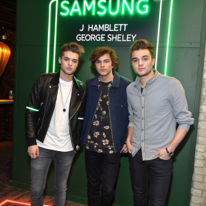 Members of Union J, JJ Hamblett and George Shelley, at a tech launch event. Dressed casually. Neon green Samsung logo backdrop.
