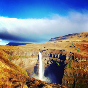 A breathtaking view of the Gasadalur Waterfall in the Faroe Islands. Majestic waterfall cascading down rugged cliffs, surrounded by lush greenery and dramatic skies.