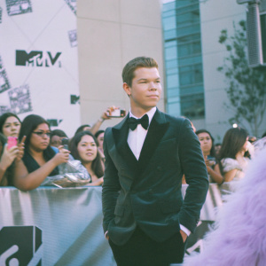 Will Poulter at the MTV Movie Awards, smartly dressed in a tuxedo. Backdrop features MTV logos, surrounded by fans and paparazzi.