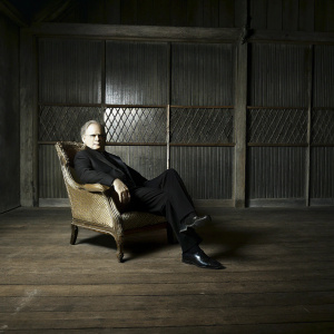 Marlon Brando in 'The Godfather', wearing a black suit, seated in a dimly lit room with wooden lattice panels. Serious expression, stern faced