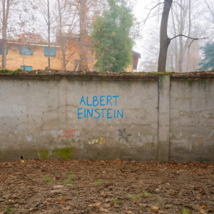 A worn concrete wall in an urban neighborhood, adorned with vibrant graffiti and a spray-painted quote from Albert Einstein.