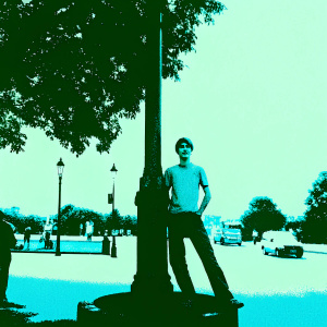 Thomas Brodie-Sangster in a casual outfit. T-shirt and jeans. Outdoors on a sunny day, near a bustling street corner