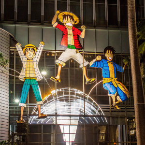 Luffy and his crew from One Piece in dynamic action poses. Brightly lit, outdoor setting with dramatic sky backdrop.