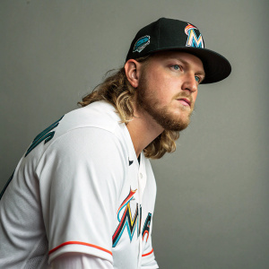 Ryne Stanek, baseball player, intense gaze. White shirt, Marlins logo, plain gray backdrop.