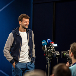 Grigor Dimitrov in a casual outfit at a press conference. Dark blue backdrop.