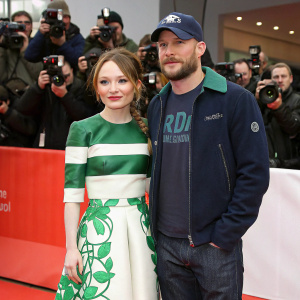 Emily Browning and Tom Hardy at the Sundance Film Festival. Emily in a vibrant green and white top with a matching skirt. Tom in casual wear, t-shirt, jacket, and cap. A sea of photographers in the background.