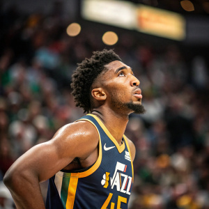 Donovan Mitchell mid-game, wearing his signature Utah Jazz jersey. Intense facial expression. Crowd blurred in background