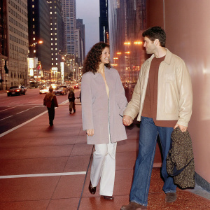 Mary Elizabeth Mastrantonio and David Giuntoli walking down a bustling city street at night, surrounded by tall buildings and bright city lights.