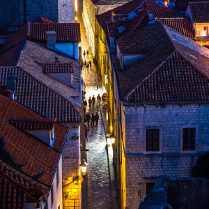 Streets of Dubrovnik's old town, Croatia. Warm sunlight casting shadows on terracotta roofs and stone walls. Earth tones dominate the scene with vibrant terracotta accents.