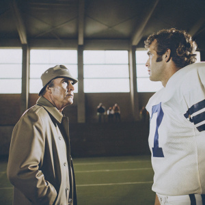 A vintage photograph captures Tom Landry, in a coaching cap, sternly looking at Roger Staubach, who wears a jersey with a large number and appears concerned, on a football field.
