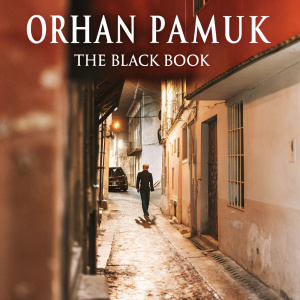 Cover art for Orhan Pamuk's 'The Black Book'. A narrow, cobblestone alley with old buildings, lone figure walking. Author and title in large font at top. Dominant colors are blue and sepia.