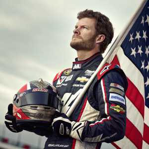 Close-up portrait of Dale Earnhardt Jr., standing in front of NASCAR flag. Dressed in racing gear