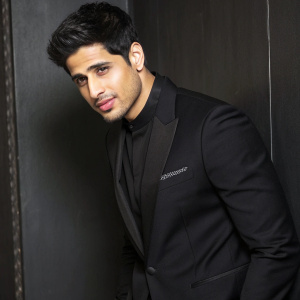 Sidharth Malhotra at the HT India's Most Stylish Awards. Wearing a black suit, looking straight at the camera. Simple, dark background.