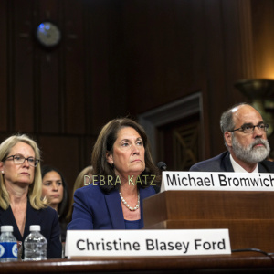 Christine Blasey Ford, Debra Katz, and Michael Bromwich in a formal senate hearing room. Dark wood table, serious expressions. Nameplate in front of Ford.