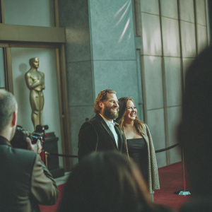 Jonah Hill and Sharon Lyn Chalkin on the Oscars red carpet. Both smiling for photographers. Oscar statue in background.