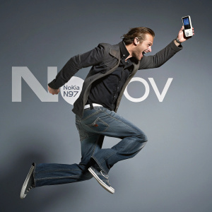 Anuncio promocional: Varón caucásico en pose dinámica en el aire. Teléfono Nokia N97. Servicio OVI. Fondo en grises.