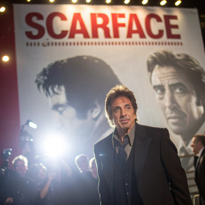 Al Pacino standing in front of a giant 'Scarface' poster. Event has bright lights and eager fans.