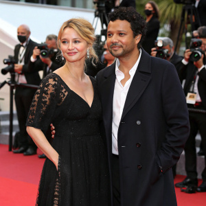 Virginie Efira and Mabrouk El Mechri attending Cannes Film Festival premiere. Efira in elegant black dress with lace details. El Mechri in dark coat and white shirt. Red carpet, flashing cameras