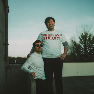 Promotional image for The Big Bang Theory merchandise. A casual photo of Sheldon Cooper and Leonard Hofstadter standing outside, wearing white t-shirts with the show's logo