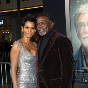 Halle Berry and Keith David, dressed in silver sequined dress and velvet blazer respectively, posing in front of Grauman's Chinese Theatre. Cloud Atlas movie poster with elderly man's face in background