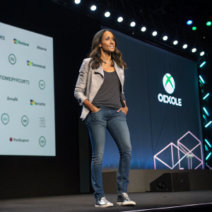 Dania Ramirez, in a casual outfit, at a tech conference. Dark stage background with brand logos