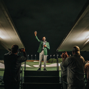 Alvaro Quiros in a green jacket, standing in a golf tournament's podium area. Surrounded by fans and photographers