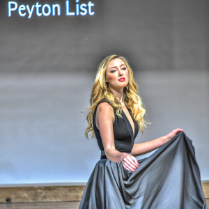 Peyton List, Caucasian actress with long blonde hair, poses in a chic black dress. Fashion event with black background and text overlay.
