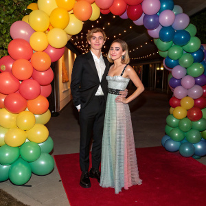 Ross Lynch and Kiernan Shipka at a fancy gala event. Balloon archway serves as backdrop. They wear formal attire and elegant dresses.