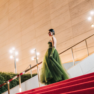 Sofia Carson at the Tini Awards in a stunning green dress. The dress has a flowing skirt and intricate details. She is standing on a red carpet with flashing lights.