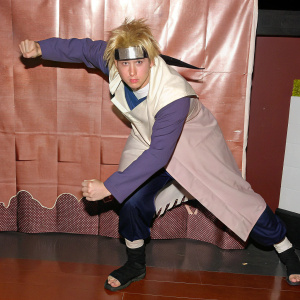 Minato Namikaze, from Naruto, depicted in action pose. Light skin, blonde hair, determined expression. Wears traditional ninja attire with white coat and blue undershirt. Digital artwork on plain black backdrop.