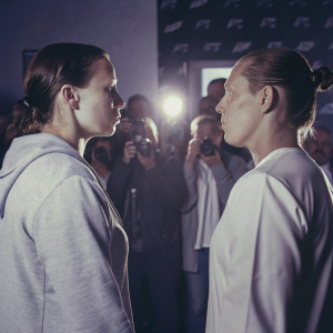 Alexis Davis and Julija Stoliarenko in intense face-off at UFC weigh-in. Crowd of photographers and fans in background.