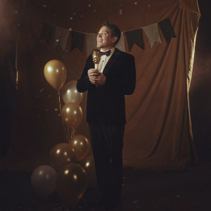 Bryan Cranston, dressed in a dark suit and bow tie, accepting an award at the Critics Choice Awards. Celebratory stage setup, banner backdrop.