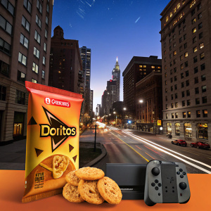 Spanish language ad featuring Doritos and cookies. Urban cityscape backdrop. Doritos bag prominently displayed with triangular shape and Nacho Cheese label. Prizes include Nintendo Switch.