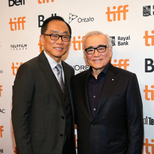 Andrew Lau and Martin Scorsese at TIFF. Andrew Lau, Asian ethnicity, in a dark suit and glasses. Martin Scorsese, white hair, dark suit, glasses. They stand in front of a wall with event logos.