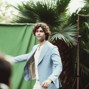 Adrian Grenier, white male with curly hair, wears a blue blazer. Poses in a studio with a green screen backdrop.