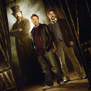 Guy Ritchie and Robert Downey Jr at a Hollywood press event. Promotional backdrop featuring Sherlock Holmes characters. Guy Ritchie in a casual outfit, Robert Downey Jr in a formal suit.