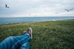 First person point of view lying on the grass on a broad field near the sea