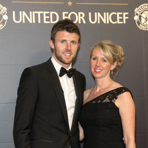 Michael Carrick and Lisa Roughead at a gala event. They are both dressed in formal attire. The backdrop features the United for Unicef logo.