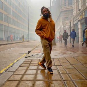 A man with dreadlocks and beard modeling casual athletic wear for Patta. On a busy street.