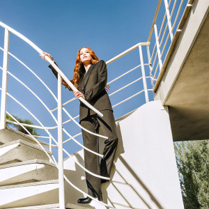 Sadie Sink, in a sleek black suit, at the Netflix FYSEE event. Dramatic lighting, minimalist black backdrop