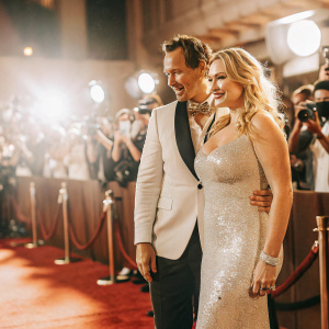 Kate Winslet and Patrick Wilson attending a glamorous movie premiere. Kate in a stunning silver sequined gown. Patrick in a stylish black tuxedo. Red carpet bustling with paparazzi and fans.