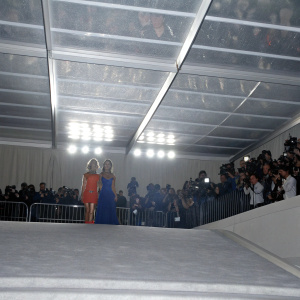 Paris Hilton and Nicole Richie attending the Met Gala. Paris in a blue gown, Nicole in an orange top. Crowded red carpet.