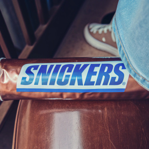 Macro shot of Snickers bar wrapper. Blue text 'Snickers' stands out on brown, shiny surface