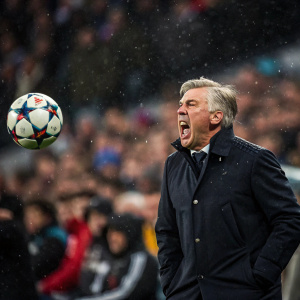 Carlo Ancelotti during a crucial soccer match. Intense facial expression, surrounded by a roaring crowd. Soccer ball mid-air.
